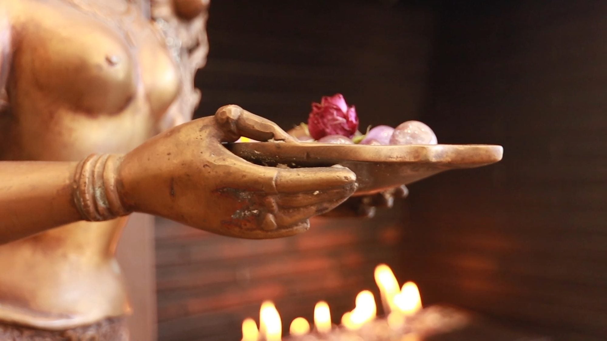 A bronze statue hand holding a rose and stones above a row of candle flames