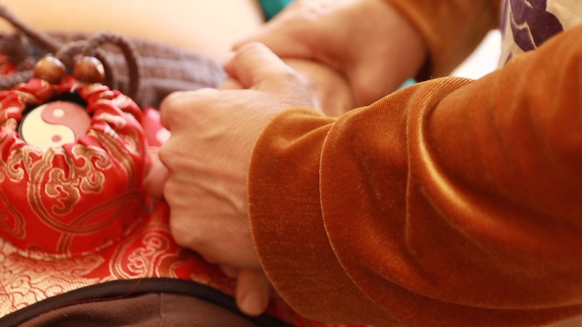 Hands in a velvet sleeve pressing a red silk castor oil pack onto a patient