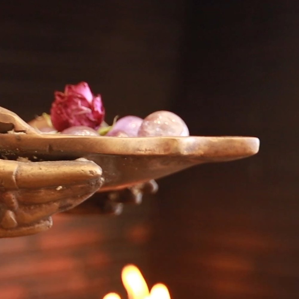 A rose and two stones rest in the open bronze palm.