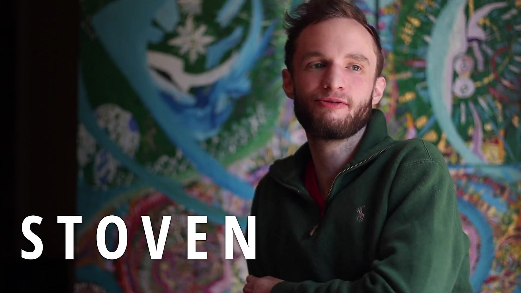 Stoven in a green pullover in front of a wall-sized painting, with the film title in white capitals