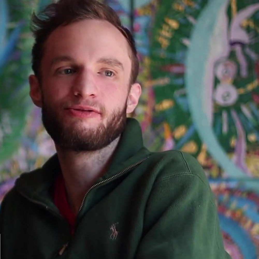 Stoven mid-sentence, the painting out of focus behind him.